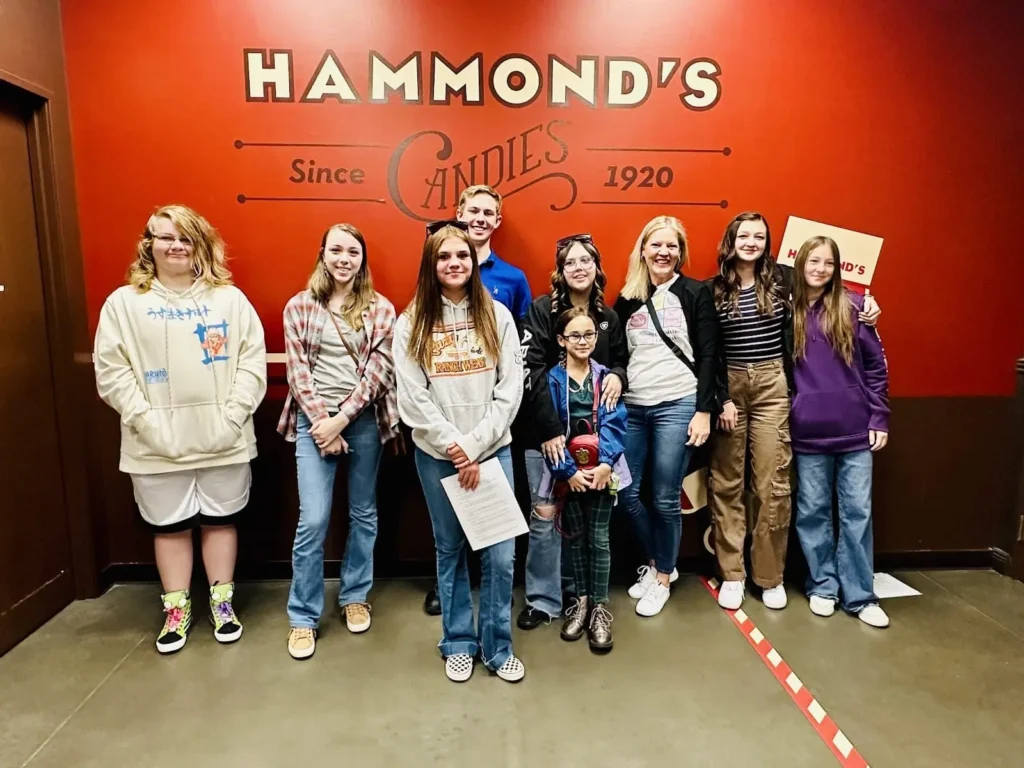 Group of eight people smiling for the camera in front of the "Hammond's Candies Since 1920" sign inside the store.